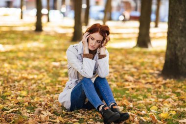 Mutsuz, üzgün, bin yıllık kızıl saçlı, yağmurluklu bir kadın, sarı yapraklı, boş bir alanda parkta oturduğunu düşünüyor. Sonbahar depresyonu, kötü haber, sadece şehir dışında stres, insanların duyguları.