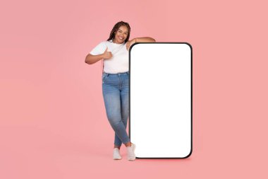 Neşeli Afro-Amerikan Kadın Cep telefonuna yaslanan Büyük Ekran Boş Hareketleriyle Pembe Stüdyo Arkaplanının Üzerinde Başvuruyu Onaylıyor. Harika bir mobil teklif. Model, Tam Uzunluk