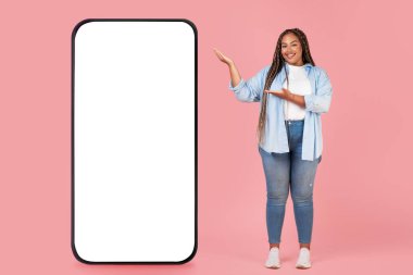 Pembe Stüdyo Arkaplanında Duran Kameraya Gülümseyen Yeni Mobil Uygulama ile Büyük Akıllı Telefon Gösteren Mutlu Siyah Kadın. Tam Uzunluk, Model