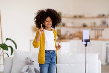 Evinden tüylü saçlı, sıradan kıyafetler giyen, dans ederken akıllı telefondan video kaydeden komik Afro-Amerikan genç kızı. Çocuk blogu, vlog kavramı