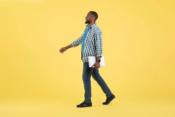 快乐的黑人男人手握手提电脑 从黄色工作室的背景中远眺过去 互联网商务和自由职业的概念 侧视图 全长镜头 — 图库照片
