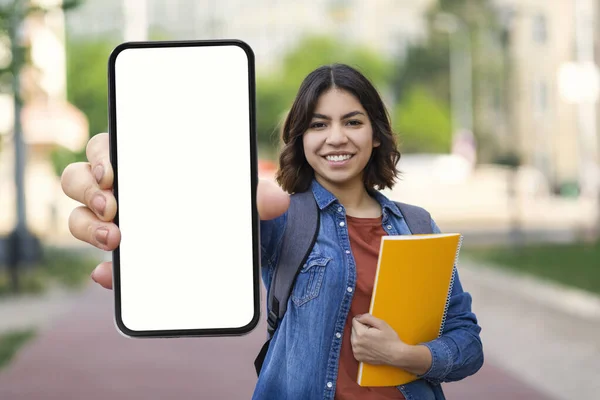 Great App. Happy Arab Student Female Showing Smartphone With Empty Screen At Camera While Posing Outdoors, Young Middle Eastern Woman Advertising New Application While Standing Outside, Mockup