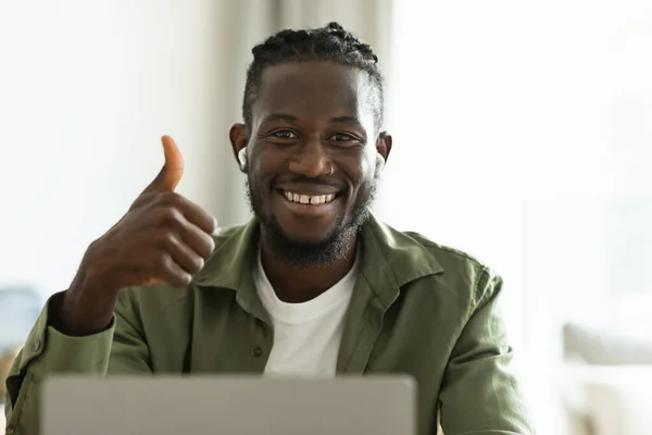 Portrait of positive african american male freelancer working on laptop and gesturing thumbs up, sitting at home office. I like freelance and entrepreneurship
