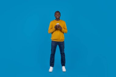 Mobil uygulama kavramı. Modern cep telefonu kullanan, mavi arka planda gülümseyen, tam uzunlukta çekim yapan ve fotokopi alanı olan bir panorama olan mutlu, Afro-Amerikan olgun bir adam.