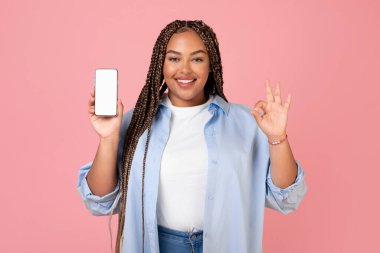 Aşırı kilolu Afrikalı Amerikalı kadın, telefon ekranı boş ve kameraya gülümseyen, pembe stüdyoda poz veren. Büyük Mobil Teklif Konsepti