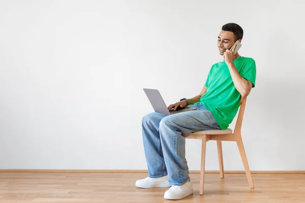 Comprimento Total Homem Usando Laptop Falando Celular Enquanto Sentado Cadeira — Fotografia de Stock