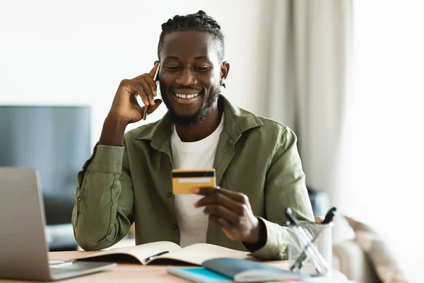 电子商务和现代银行服务的概念 快乐的非洲裔美国人 拿着信用卡 在电话里交谈 打电话到自己的银行 坐在总公司的工作岗位上 — 图库照片