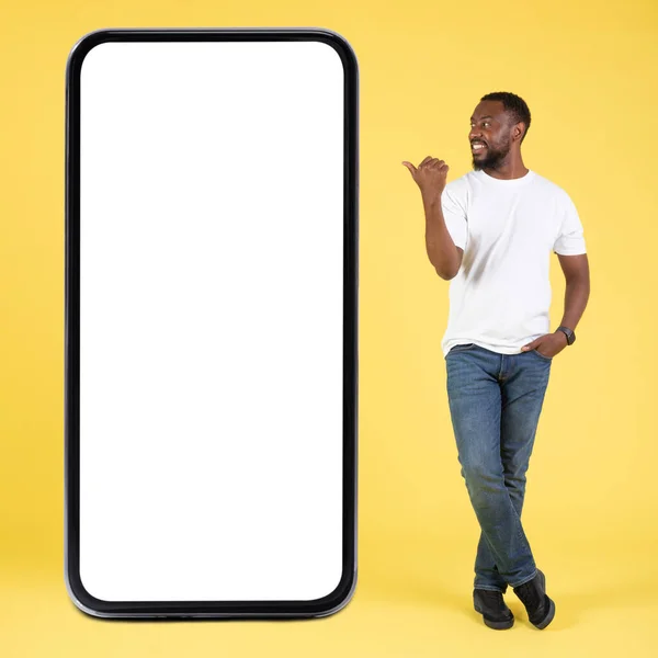 快乐的非洲裔美国人靠近大手机指尖大屏幕上的拇指手指站在黄色工作室背景下的空屏幕广告手机 电话的巨大应用 正方形射击 — 图库照片