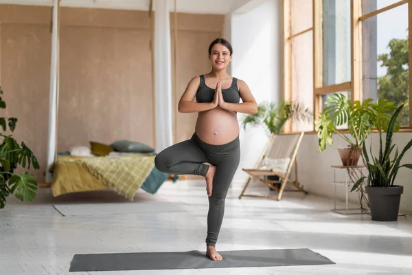 美丽的年轻孕妇在家练习瑜伽 站在树桩里 快乐迷人的孕妇在客厅里学习健身垫 享受家庭锻炼 复制空间 — 图库照片