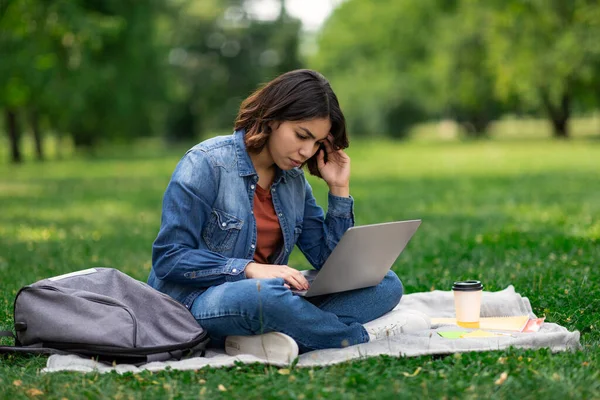 Upset Arab Female Student Using Laptop While Sitting On Plaid In Park, Young Middle Eastern Woman Study With Computer Outdoors At Campus, Having Problems With Distance Learning, Copy Space