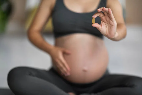 Pregnancy Vitamins. Cropped shot of pregnant female with pill capsule in hand, unrecognizable expecting woman recommending supplements for health and beauty, selective focus, closeup
