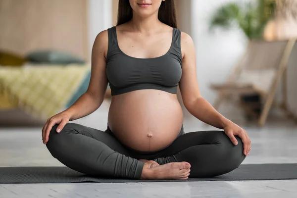 妊娠中の若い女性の作物のショットは 自宅でヨガマットに座ってアクティブウェアで ロータス位置で裸腹瞑想と認識できない期待の女性 妊娠中の瞑想を練習 — ストック写真