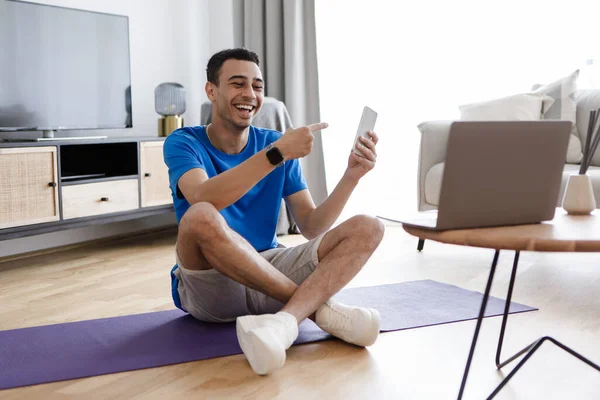 解决程序 快乐的男性健身博客向笔记本电脑摄像头展示智能手机 推荐应用程序用于培训 在线技术 体育用品 — 图库照片