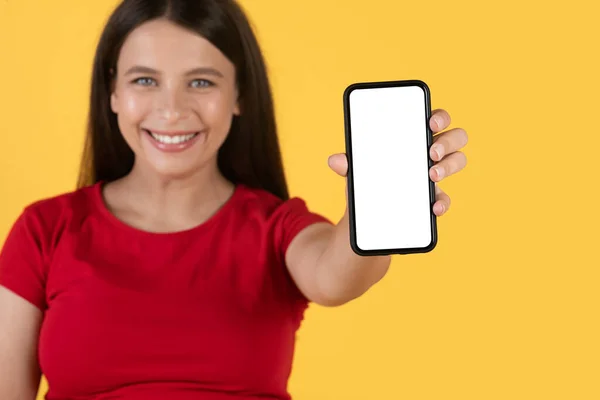 モバイルオファー 黄色の背景に隔離されながらカメラで白い画面が空のスマートフォンを示す幸せな美しい妊娠中の女性 コピースペースを示す笑顔の女性 モックアップ — ストック写真