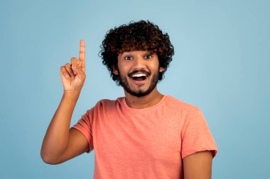 Eureka, jest konsepti. Heyecanlı, bin yıllık pembe tişörtlü yakışıklı Hintli adam işaret parmağıyla mavi stüdyonun arka planında gülümsüyor, güzel bir fikri var.