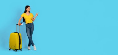 Sarı tişörtlü güzel Japon bayanın pasaport tutmasına, uçak biletlerine, boş alanı göstermesine, mavi arka planda izole edilmesine sevindim. Seyahat, reklam ve teklif, insani duygular, covid-19 sonrası yolculuk