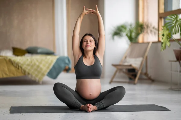 怀孕瑜珈 安详美丽的怀孕妇女舒展健康舒适的坐姿在家 微笑宁静期待的女性坐到荷花的位置 举起双臂 享受健康的生活方式 复制空间 — 图库照片
