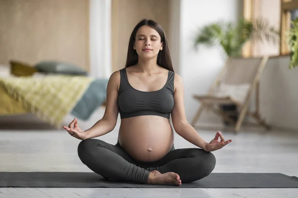 年轻怀孕女性在家用瑜伽垫冥想的肖像 荷花姿势坐着用动作片的漂亮孕妇 客厅室内练习冥想 — 图库照片