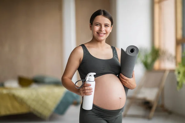 妊娠活動 ヨガマットと手の中に水ボトルと笑顔妊娠中の女性の肖像 自宅のインテリアにポーズ陽気若い期待の女性 スポーツトレーニングの準備ができて スペースをコピー — ストック写真