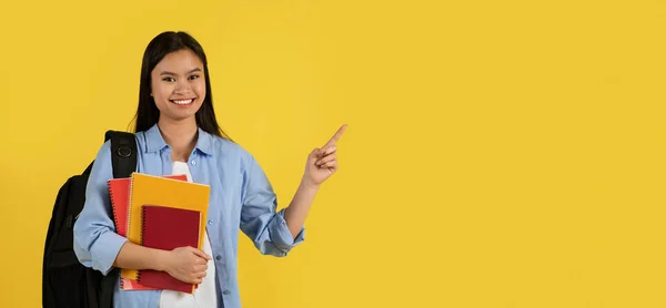 穿着休闲装的年轻中国女学生笑着 背包和许多书都指向空旷的空间 孤立在黄色的背景下 学习和教育 广告和提供适当的合作D — 图库照片