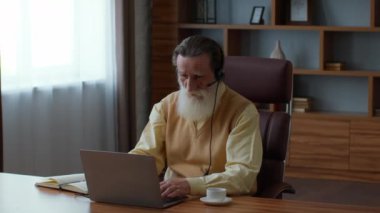 Yaşlılık ve iş. Üst düzey sakallı adam, ortaklarla dizüstü bilgisayarla görüşüyor, projeyi tartışıyor ve notlar alıyor, izleme çekimi, yavaş çekim, serbest alan