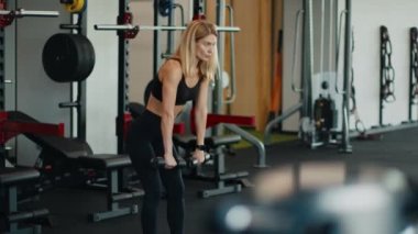 Spor vücut egzersizi. Aktif kadın atlet halterlerle eğiliyor, spor salonunda çalışıyor, çekim takibi, yavaş çekim, serbest alan