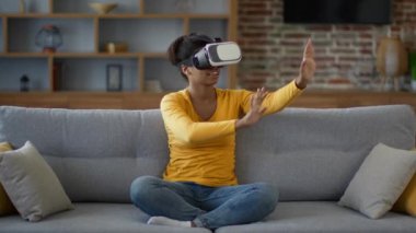Sanal eğlence. Genç, mutlu, Afro-Amerikan kadın oyuncu video oyunlarından zevk alıyor, VR kulaklıkla, görünmez tuşlara basıyor, siber dünyanın tadını çıkarıyor, yavaş çekim, serbest alan