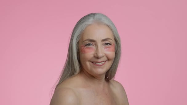 护肤化妆品积极的高个子灰发女士 有胶原蛋白斑块 脸转向相机和微笑 粉红工作室背景 慢动作 — 图库视频影像