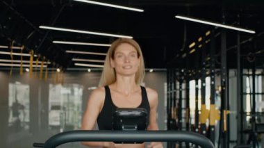 Sabah koşusu egzersizi. Modern jimnastik salonunda koşu bandında koşan mutlu orta yaşlı kadın portresi, yavaş çekim.