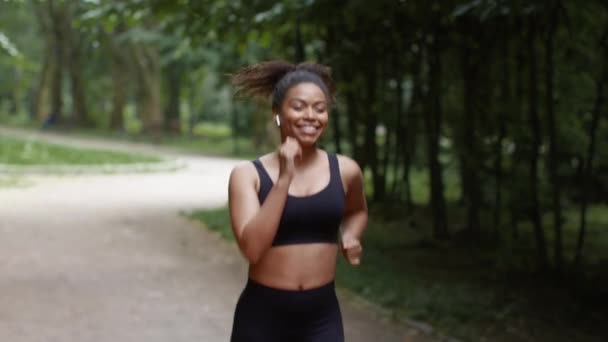 心情很好的来源 年轻快乐的非洲裔美国女慢跑者 早上在公园里跑步 听着耳边的音乐 跟着镜头 慢动作 — 图库视频影像