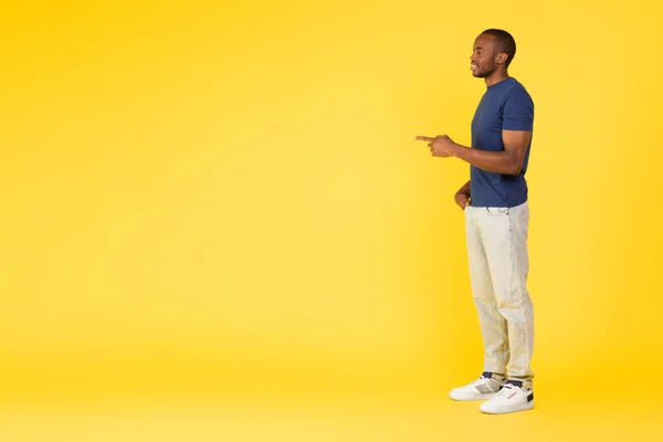 看那里 从侧面看非裔美国男性指向空白处的手指广告提供站在工作室黄色背景之上 — 图库照片