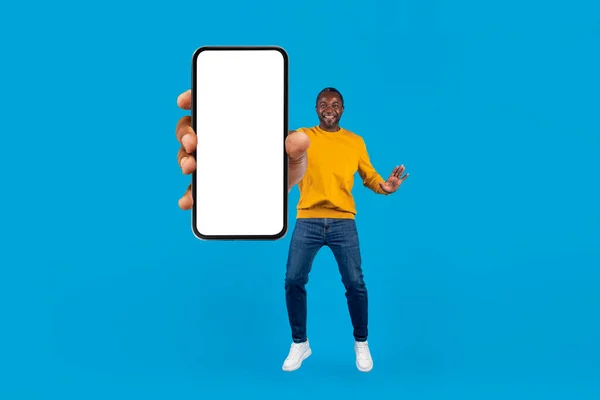 快乐而兴奋的中年非洲裔美国男人 穿着时髦的休闲装 展示着带有白色空白屏幕的现代智能手机 在蓝色工作室的背景 复制空间和全长上跳舞 — 图库照片