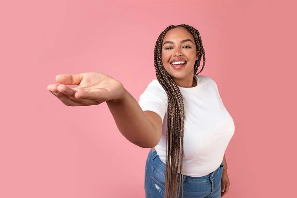 Happy Black Overweight Lady Showing Hand To Camera Advertising Invisible Product Standing In Studio Over Pink Background, Smiling To Camera. Advertisement Template Concept