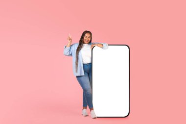 Siyah Kadın, Pembe Stüdyo Arkaplanındaki Boş Ekran Pozunu Yandan Gösteren Büyük Cep Telefonu 'nun yanında duruyor. Artı Boyut Kadın Reklam Mobil Uygulaması. Tam Uzunluk, Model