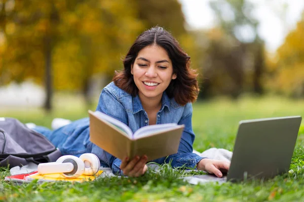 美丽的阿拉伯女学生 带着书本和笔记本电脑在户外学习 微笑着躺在公园草坪上的中东女人 准备考试和放松自己 用自由的空间拍摄衣服 — 图库照片