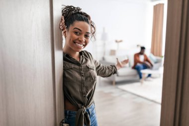 Hoş geldiniz. Mutlu Afrikalı Amerikalı kadın sizi evdeki oturma odasında el ele tutuşmaya davet ediyor. Gayrimenkul ve Kira Konsepti. Seçici Odaklanma