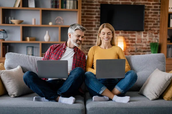 微笑的欧洲中年男子看着女士的笔记本电脑 聊着天 享受着闲暇时光 坐在客厅的沙发上 用于视频通话 工作和上网的设备 好的广告和提供服务 — 图库照片