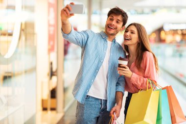 Mutlu Alıcılar çift alışverişi yapıyor selfie çekiyor ve modern alışveriş merkezinde eğleniyor. Müşteriler alışveriş torbalarıyla poz veriyor. Satış sezonunda Hypermarket 'te vakit geçiriyorlar. Seçici Odaklanma