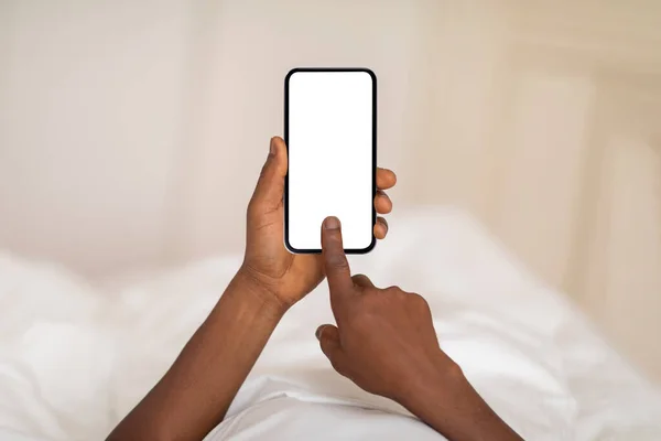 Unrecognizable Black Man Touching Blank Smartphone Screen While Lying Bed — стоковое фото