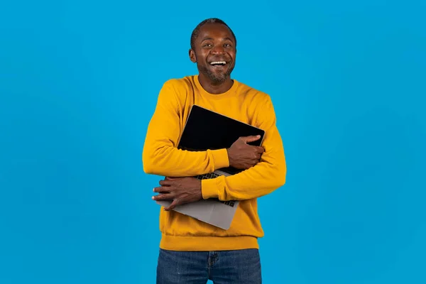 笑着可笑的中年非洲男人抱着打开的现代笔记本电脑 摆出蓝色的工作室背景 复制空间 现代小玩艺儿 电脑成瘾概念 — 图库照片