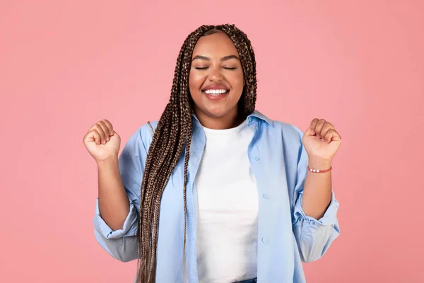 Happy African American Overweight Lady Shaking Fists In Joy Posing With Eyes Closed Standing Over Pink Studio Background. Success And Happiness, Victory Celebration Concept