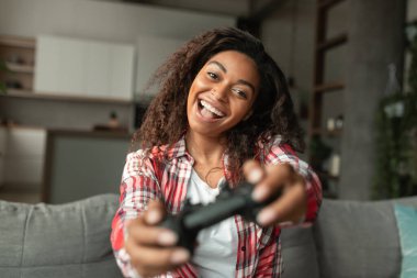 Ağzı açık bir şekilde oyun oynayan, oturma odasındaki kanepede oturan heyecanlı Afro-Amerikalı bir kadının oturmasına sevindim. Evde tek başına eğlenmek, karantinaya alınması gereken eğlence.