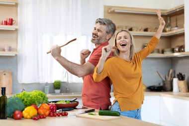 Duygusal olarak çekici orta yaşlı karı koca evde yemek pişirirken eğleniyorlar, mutlu eşler yemek hazırlıyorlar ve şarkı söylüyorlar, mutfak içi, kopyalama alanı.