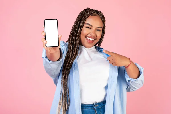 幸せなアフリカ系アメリカ人女性がピンクの背景に指を指して携帯電話の空の画面を表示します 女性広告偉大なアプリケーションまたは提供 スタジオショット モックアップ — ストック写真