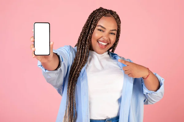 明るい黒の女性は ピンクのスタジオの背景の上に立ってカメラに笑顔でスマートフォンを指して 素晴らしいモバイルオファーとアプリケーション広告コンセプト — ストック写真