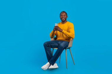 Rahat, orta yaşlı, rahat, siyah bir adam. Mavi stüdyo arka planında oturuyor. Cep telefonu kullanıyor, internette sörf yapıyor, arkadaşlarıyla sohbet ediyor.