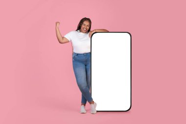 Pembe Stüdyo Arkaplanı Üzerine Evet Hareketi yapan Büyük Akıllı Telefonun yanında Büyük Siyah Kadın Poz Veriyor. Mobil Uygulama Reklamı. Mockup, Tam Uzunluk Çekimi