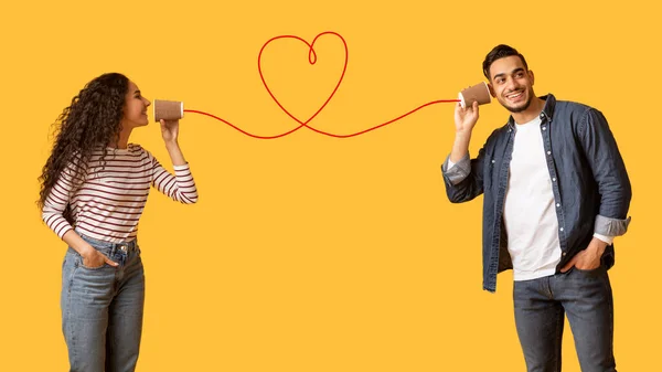 Romantic Arab Woman Sending Love Message To Boyfriend Through Paper Cup Phone With Heart Shaped String, Affectionate Couple Standing Together Isolated Over Yellow Background, Collage