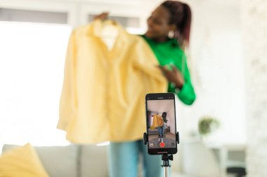 Modern moda blogcusu başarılı alışverişin ardından yeni kıyafetlerle video eleştirisi yapıyor, akıllı telefondan video kaydediyor, tripoda cihaz takıyor, seçici odaklanıyor. Blogculuk kariyeri