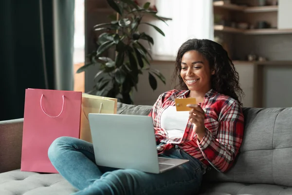 100万人ものアフリカ系アメリカ人女性がノートパソコンとクレジットカードを持ち リビングルームのインテリアに多くのパッケージがあるソファに座っています オンラインショッピング 巨大な販売 自宅での配信 素晴らしい広告やオファー — ストック写真